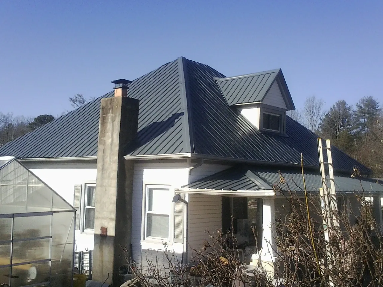 Dark blue standing seam metal roof on a white farmhouse with dormer — Slate & Tile Roof Repair by Roofing Brothers in Deer Park
