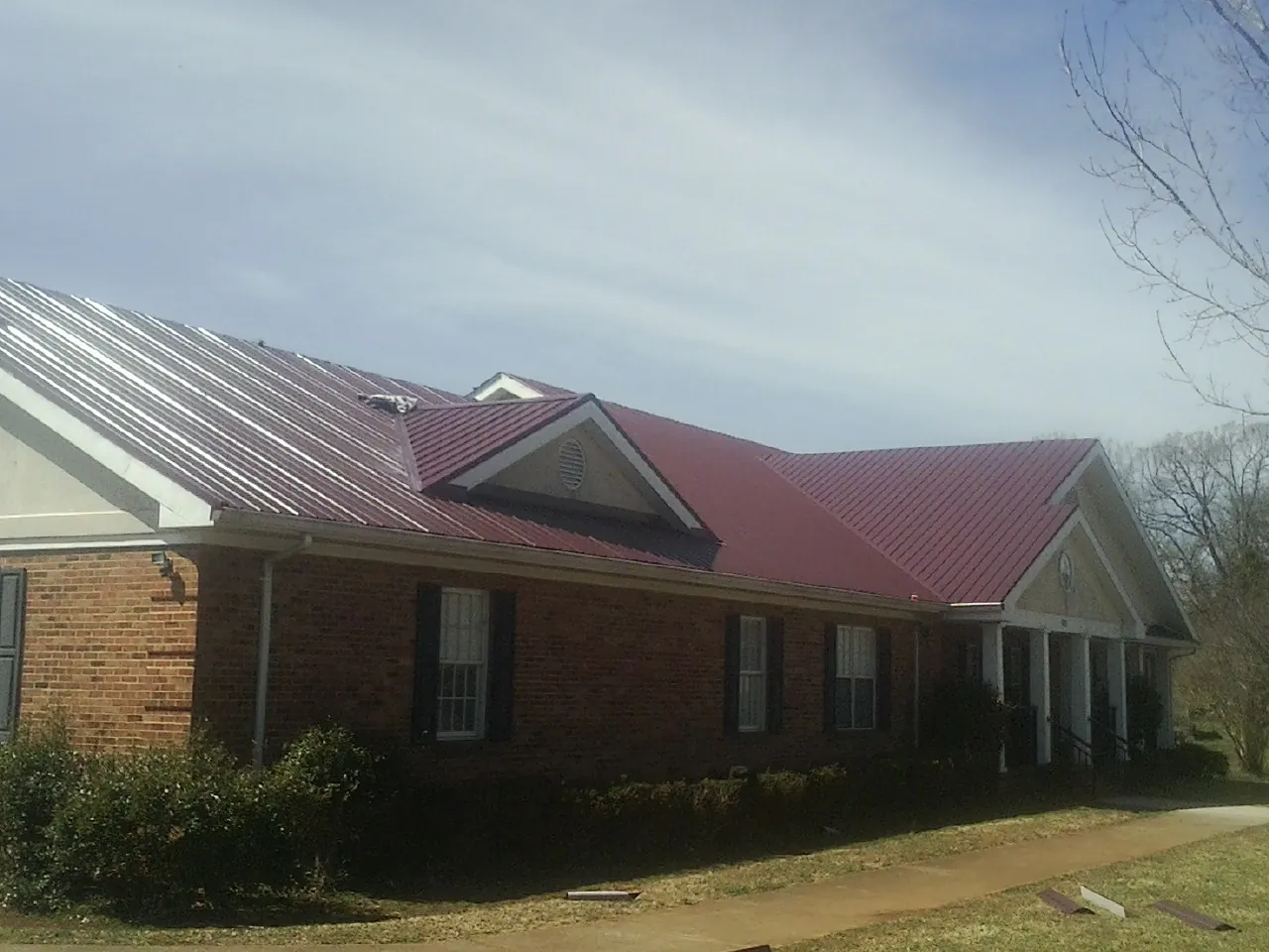 Red metal roof with gabled entries on a long brick building, from a Hail Damage Roof Repair job in Deer Park