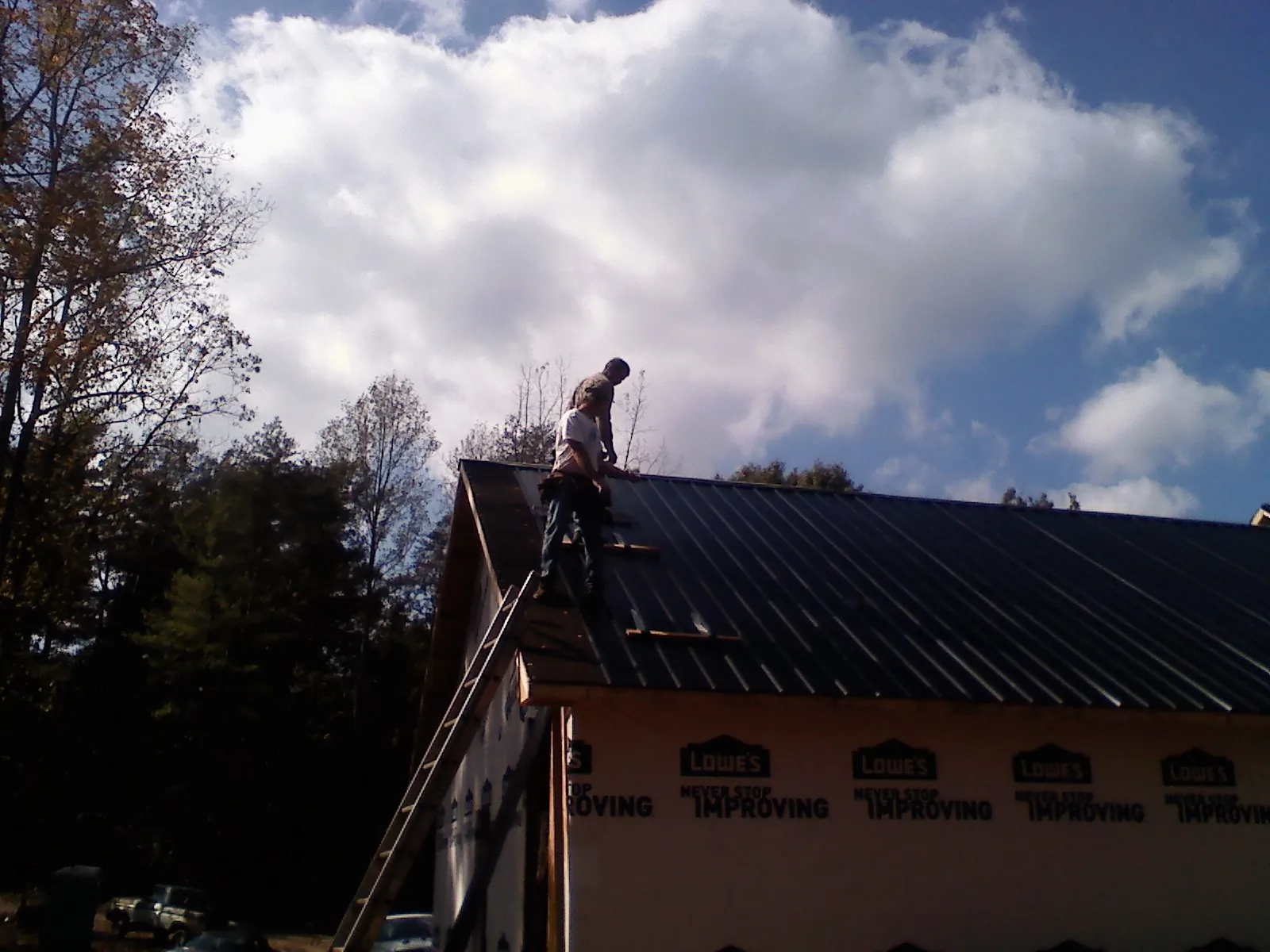 Roofer fastening dark metal panels high against a cloudy sky, from a Roof Inspection job in Deer Park